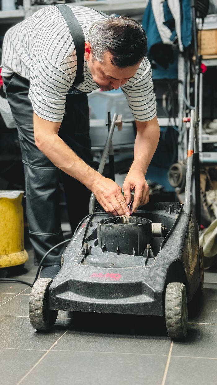 About Adult repairing a lawn mower in a garage workshop, focused on maintenance and DIY repair.